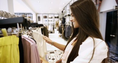 Junge Frau mit langen braunen Haaren stöbert durch Kleidung in einem Geschäft in Saarbrücken