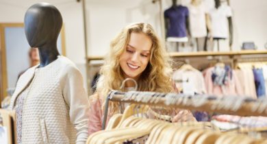 Junge blonde Frau als Kunde beim Shopping nach Kleidung in einem Modeladen